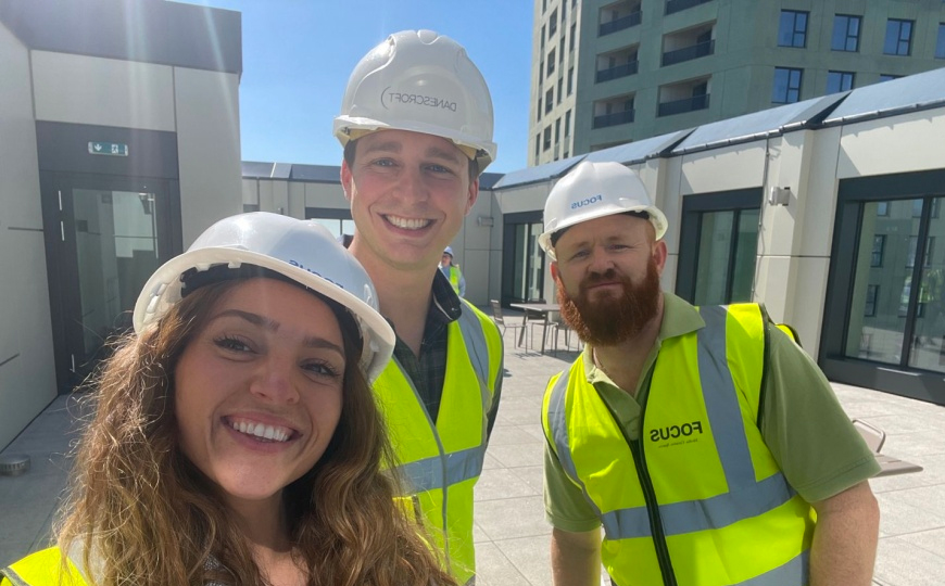three people on a construction site taking a selfie wearing high-vis jackets and hard hats