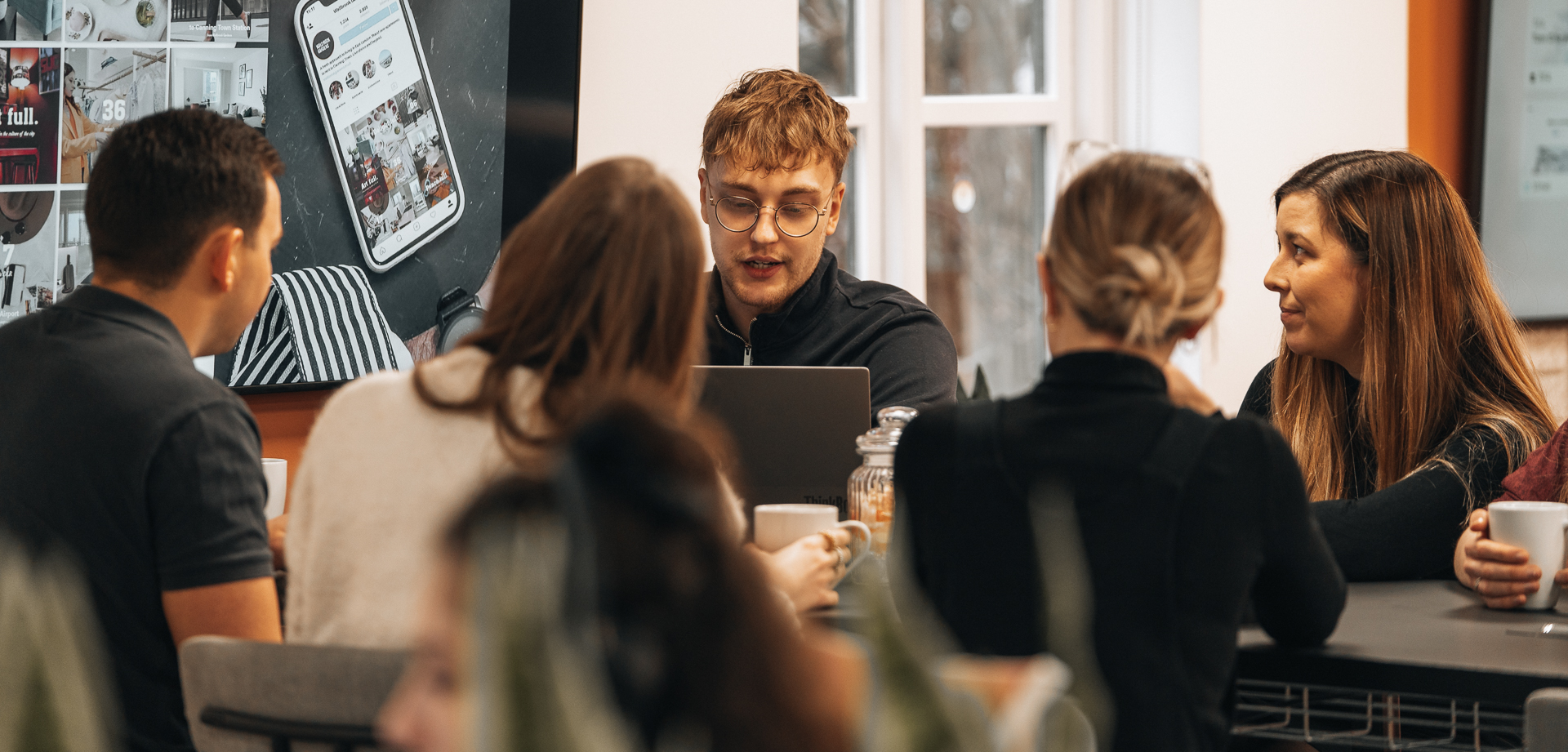 Group of young people sat around a desk with coffee talking