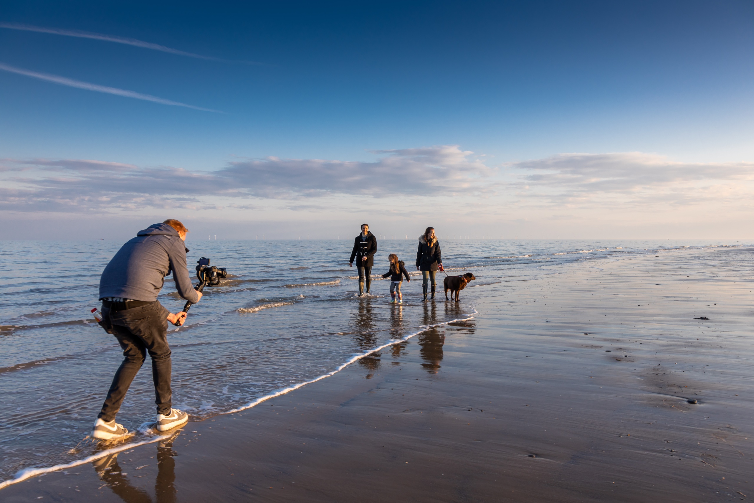 Man filming a Family walking along the beach with their dog