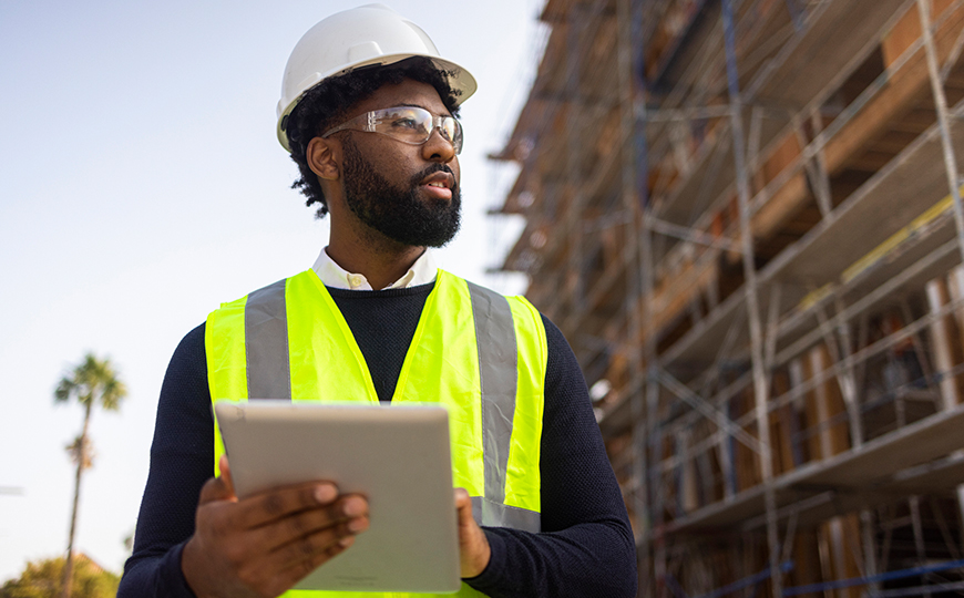 Man on a construction site wearing various types of PPE such as a high-visibility jacket and a hard hat