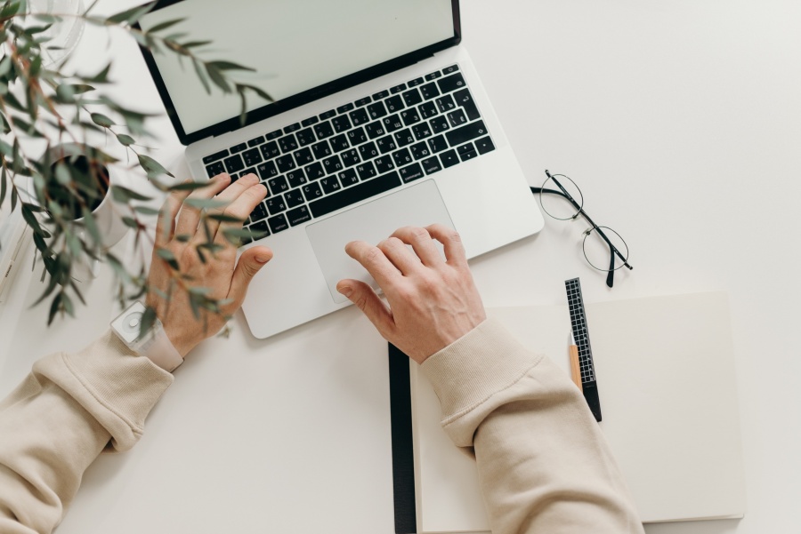An individual at a white desk typing on their laptop