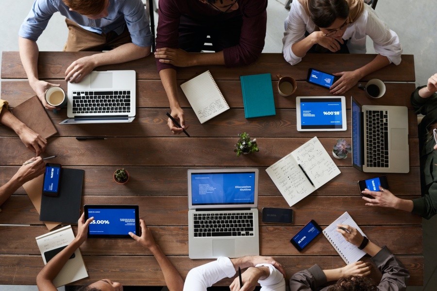 A group of business people having a meeting around a wooden table taking notes on laptops and notepads