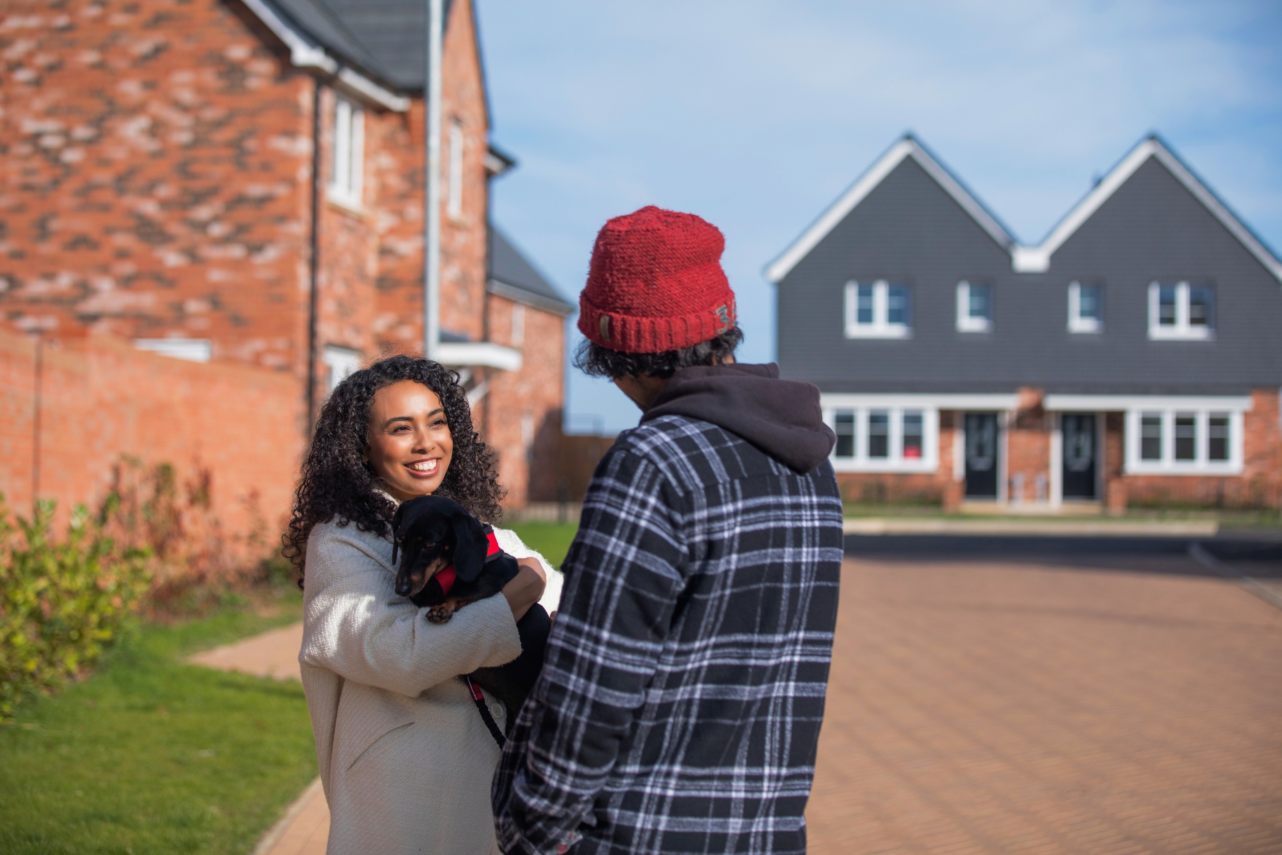 A smiling couple stood in front of their homing holding their dog