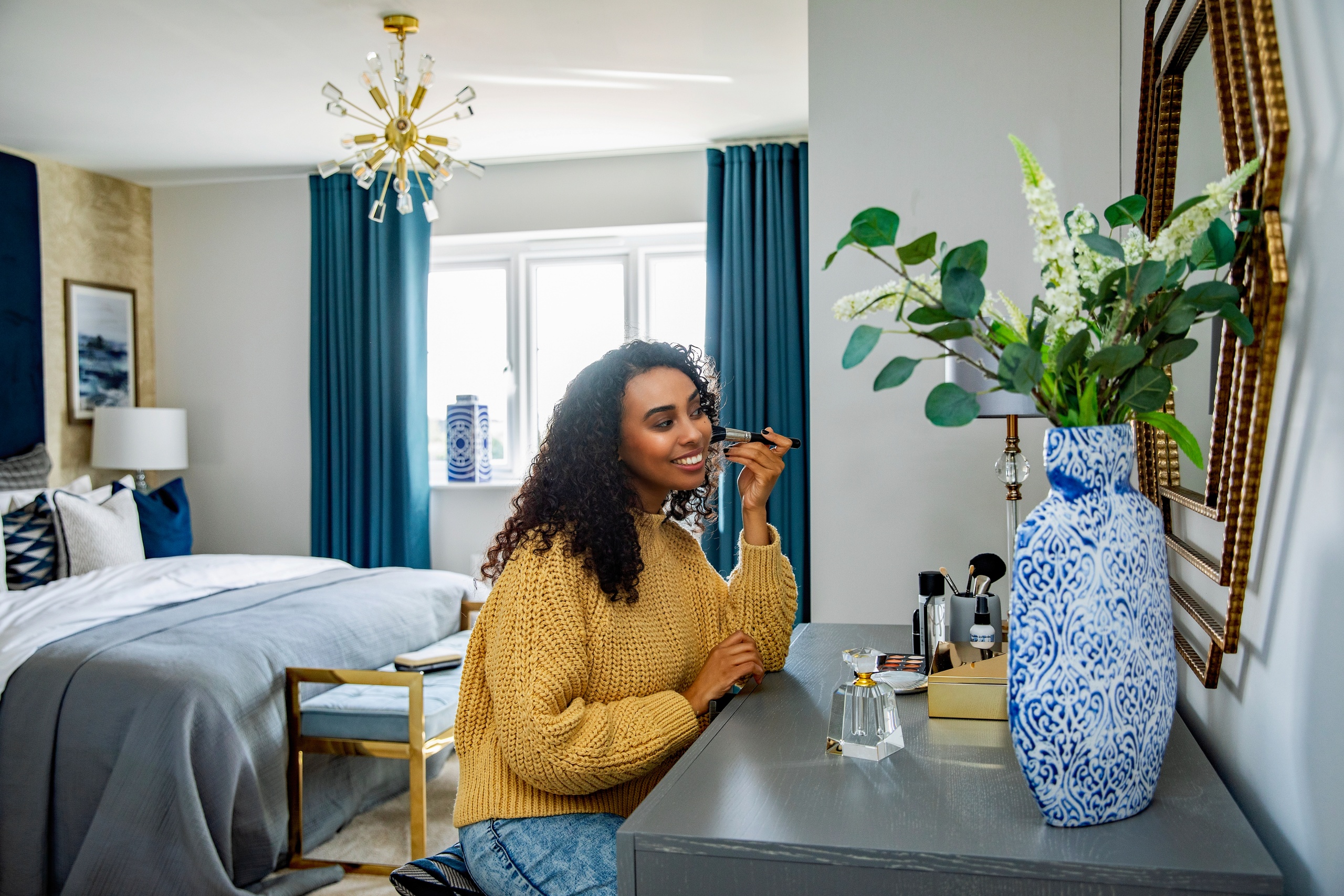 A woman in her bedroom putting makeup on in front of a large mirror