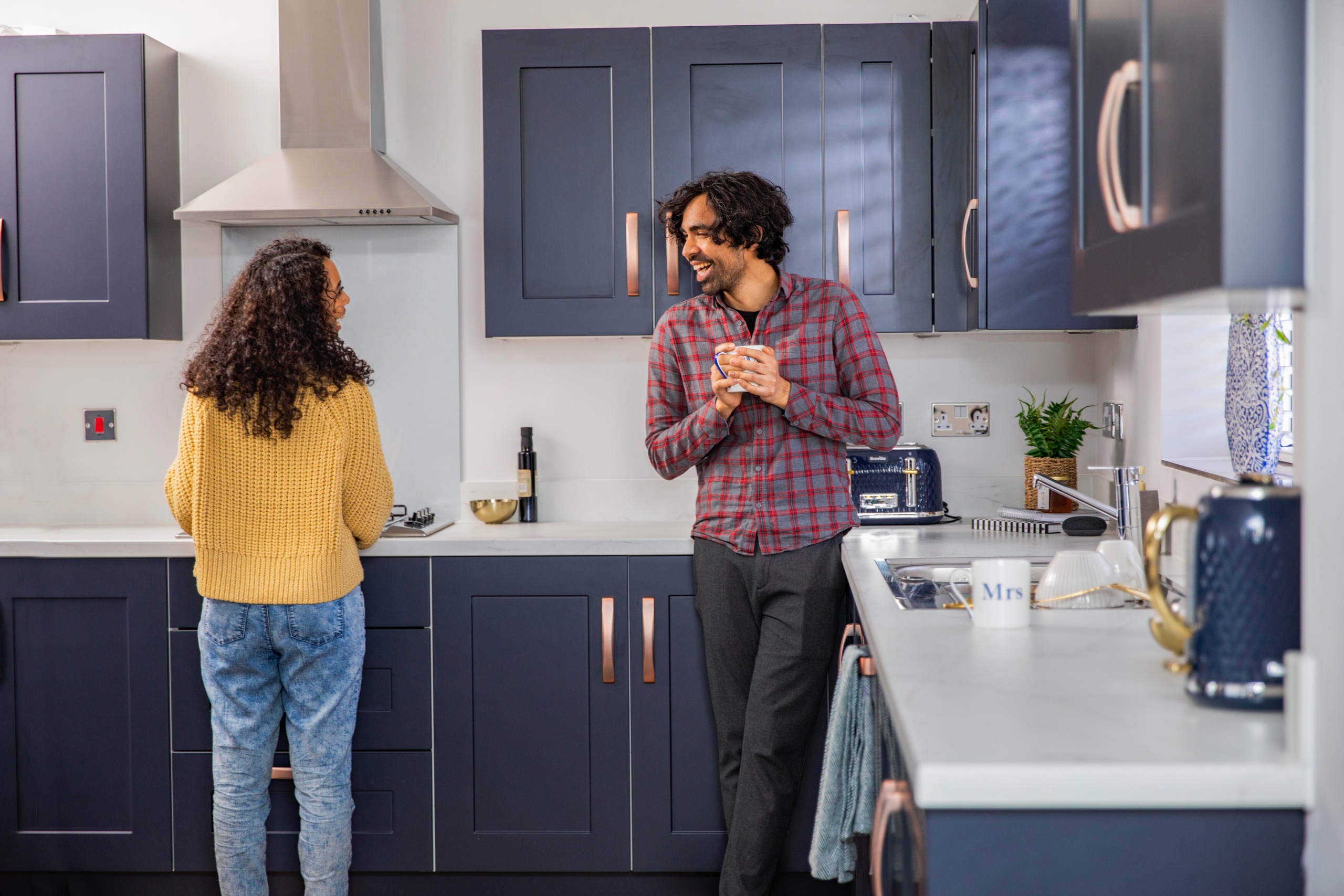 A couple stood in the kitchen laughing together while the women is cooking