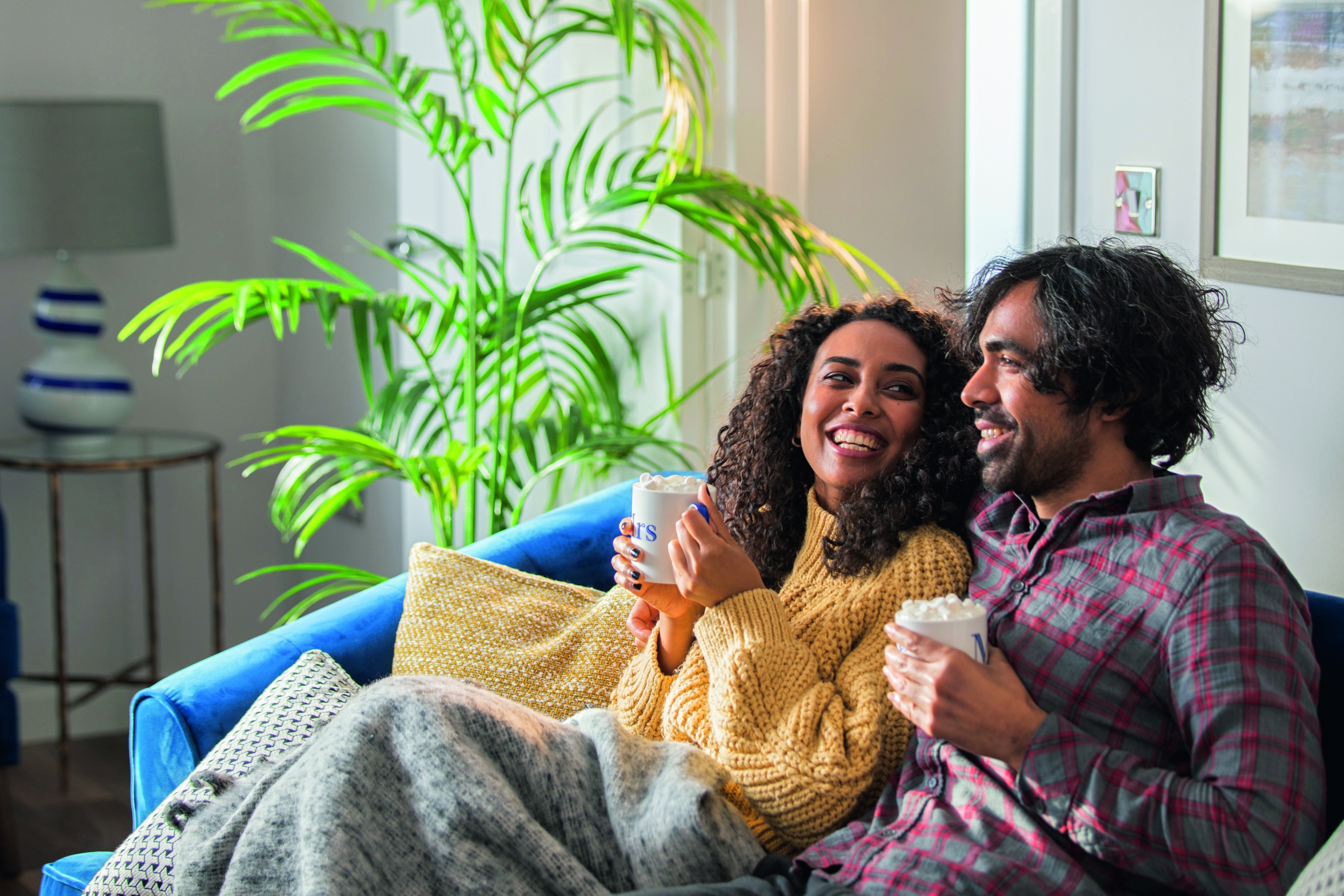 A happy couple cuddling on the sofa drinking hot chocolate