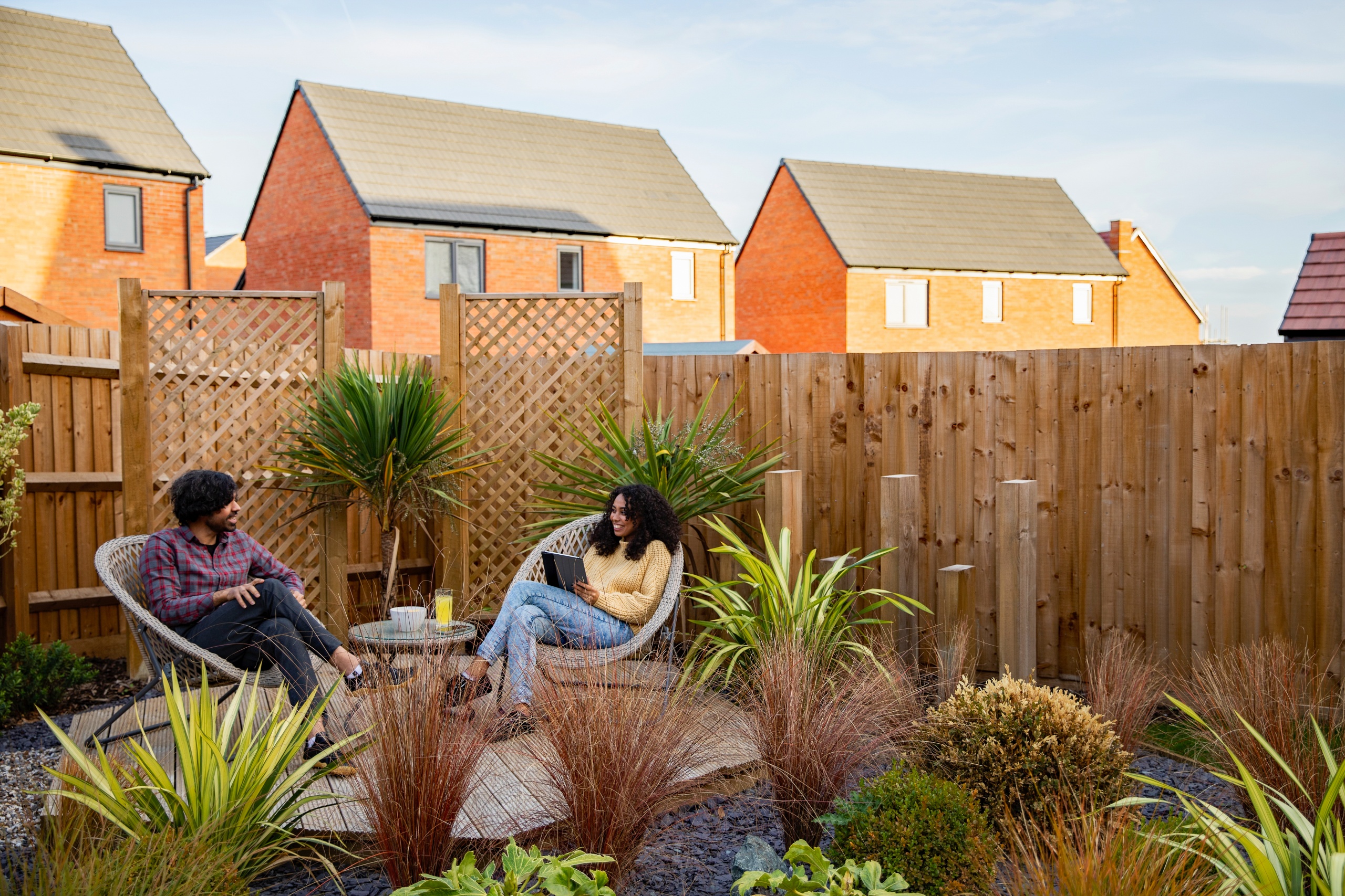 A couple chatting sat in their garden that is full of plants and bushes