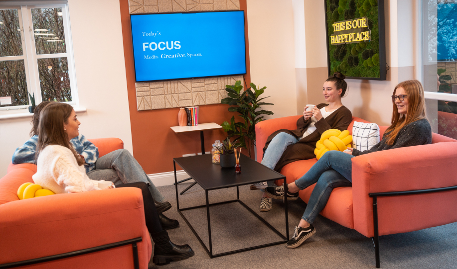 Group of friends sat on sofas talking and drinking coffee