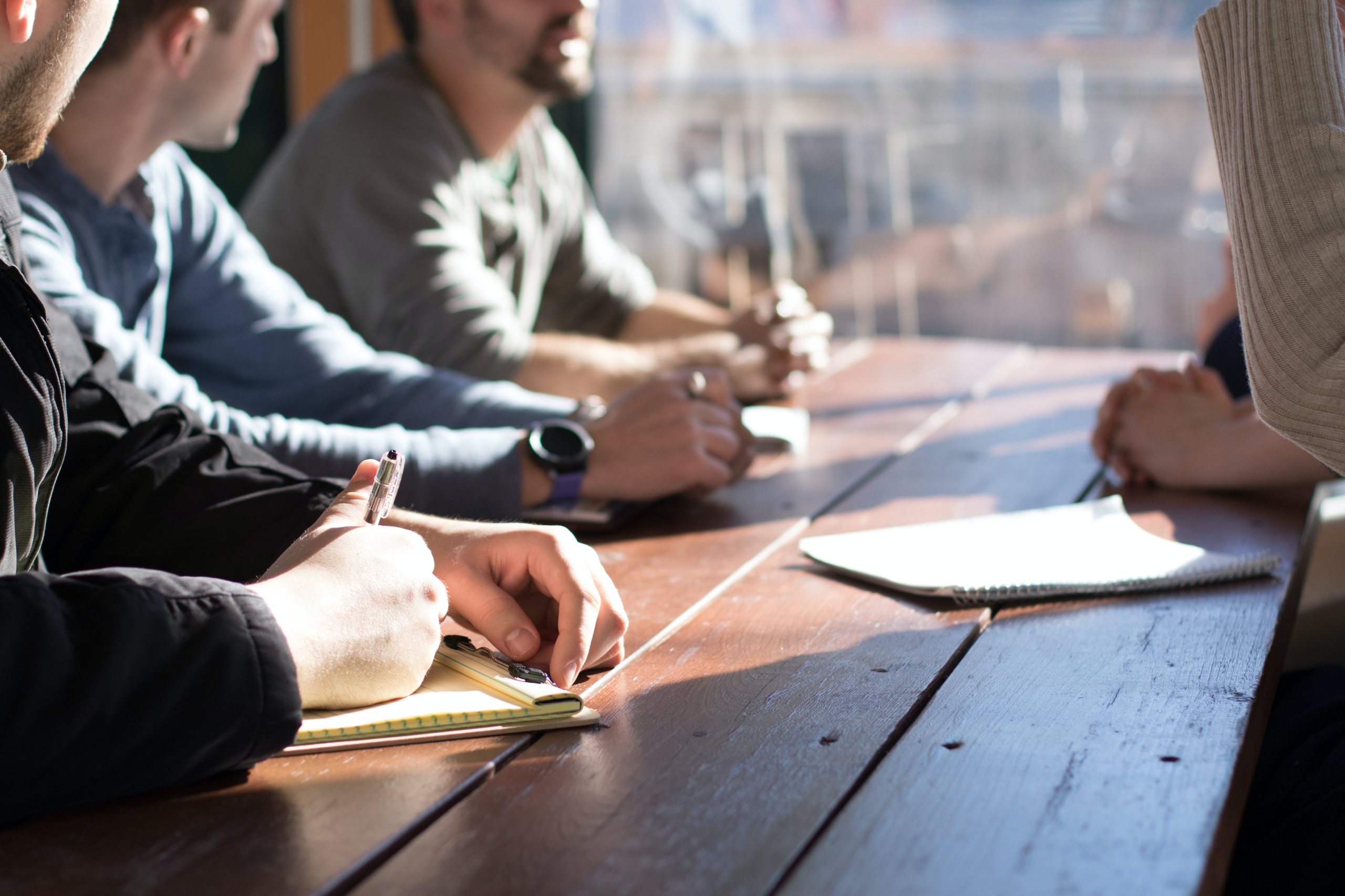 Group of people sat at a wooden bench with note pads talking