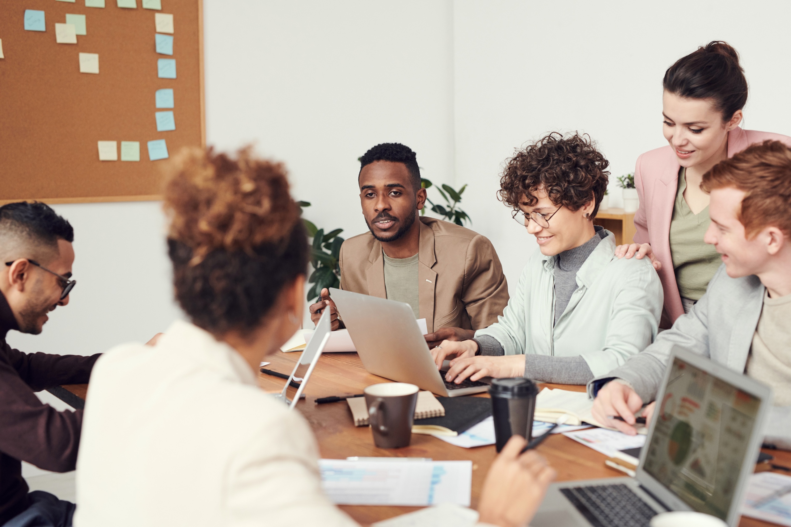 Group of several business men and women sat around a desk chatting with their laptops