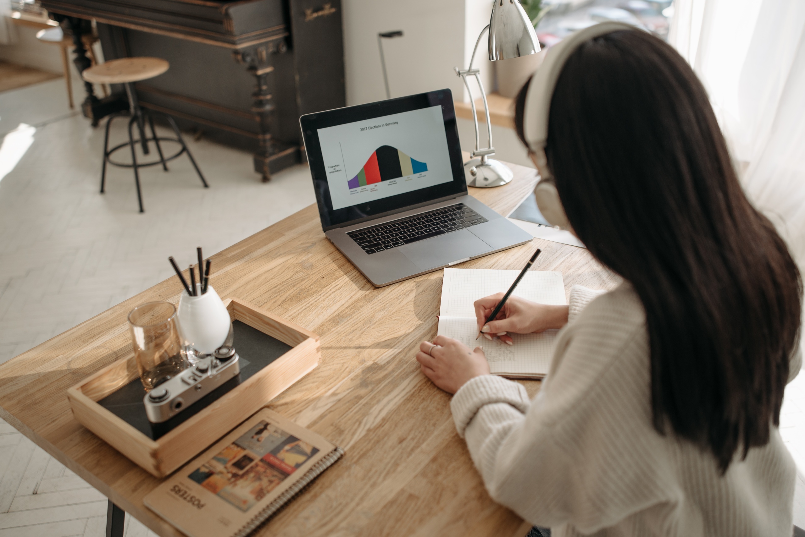 Women sat at her desk with headphones on taking down notes on to a pad off of her laptop