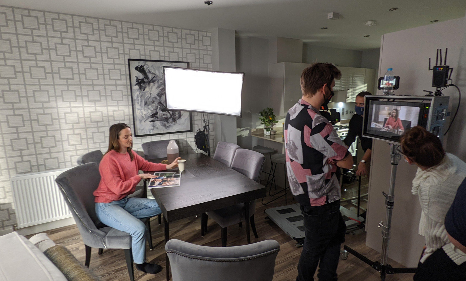 lady sat at a table reading a magazine being recorded by a camera crew
